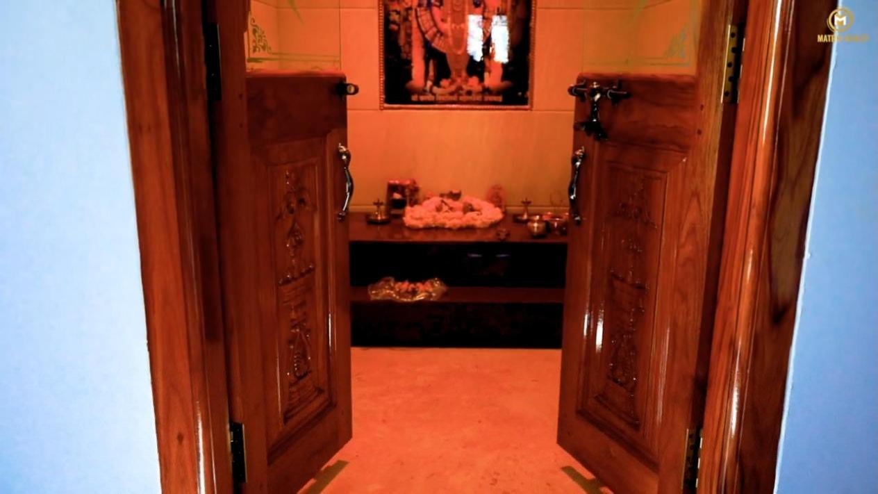 Pooja room with carved teak double doors in the Hassan duplex house